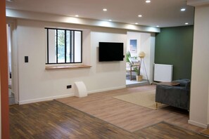 Uma sala de estar moderna com uma TV de tela plana, uma janela com persianas, um sofá cinza e um radiador.