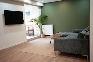 Un salon moderne avec un canapé gris, un téléviseur à écran plat, une plante en pot et un plancher en bois.