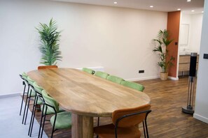 Uma sala de conferência com uma longa mesa de madeira, cadeiras estofadas verdes e plantas em vasos.