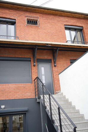 Um edifício de dois andares com fachada de tijolos, escada de metal e porta de garagem.
