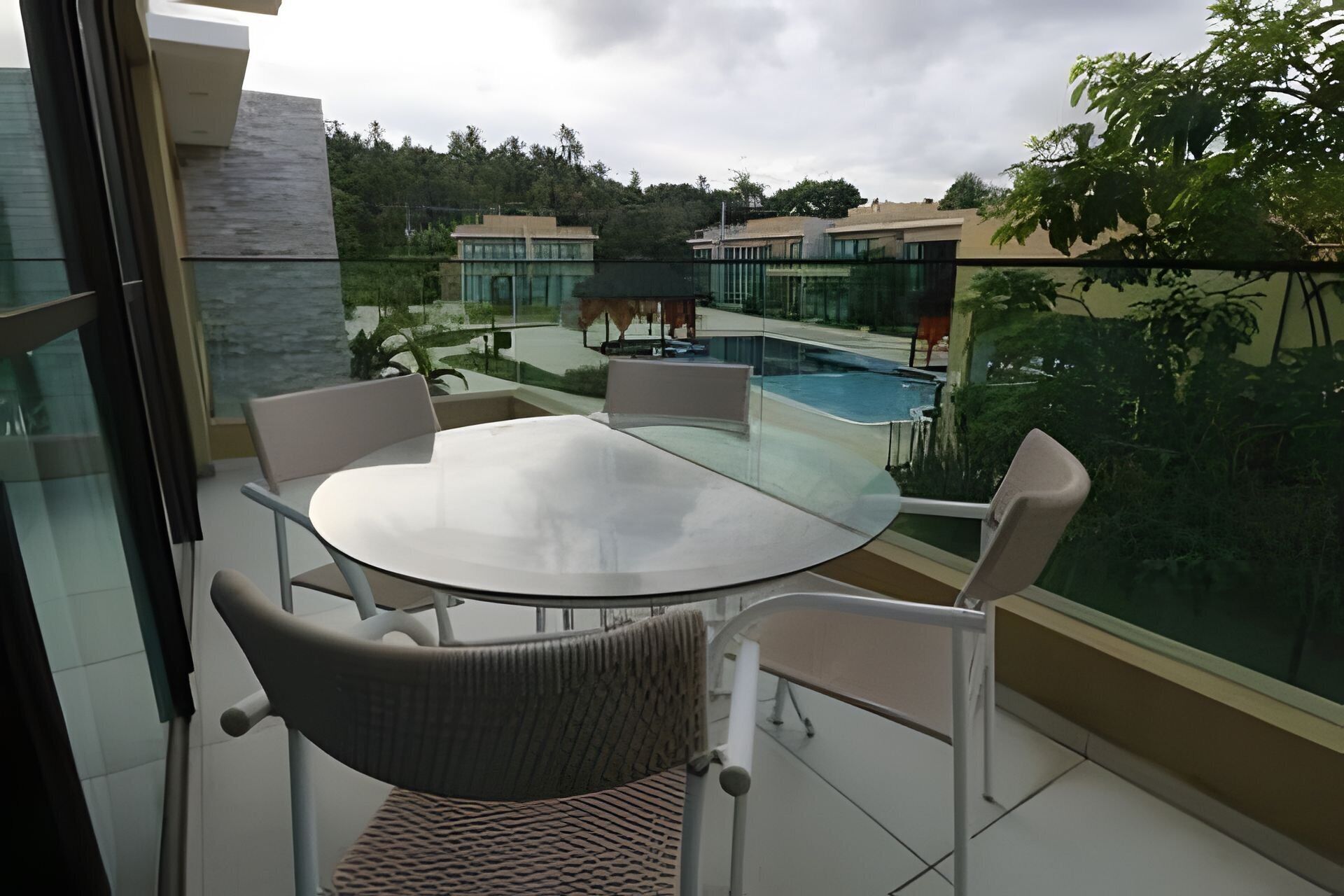 Ein Balkon mit Glastisch und Stühlen, mit Blick auf einen Swimmingpool und Wohnhäuser.