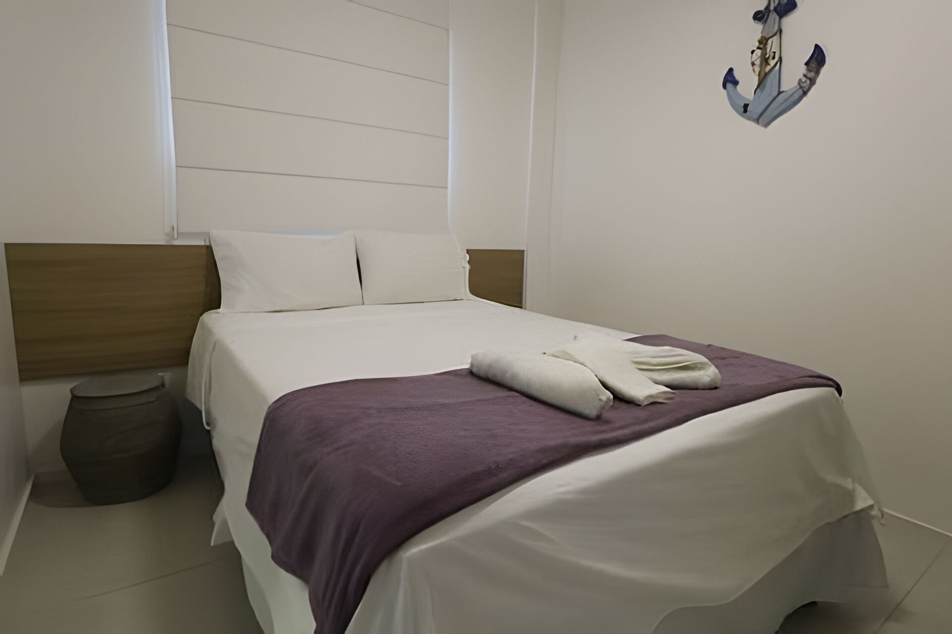 Et soveværelse med seng, puder, et natbord og en dekorativ anker på væggen.