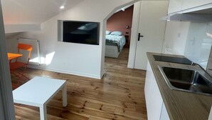 Una cucina moderna con forno integrato, un'area pranzo con tavolo bianco e sedie arancioni, e una camera da letto con letto e televisione.
