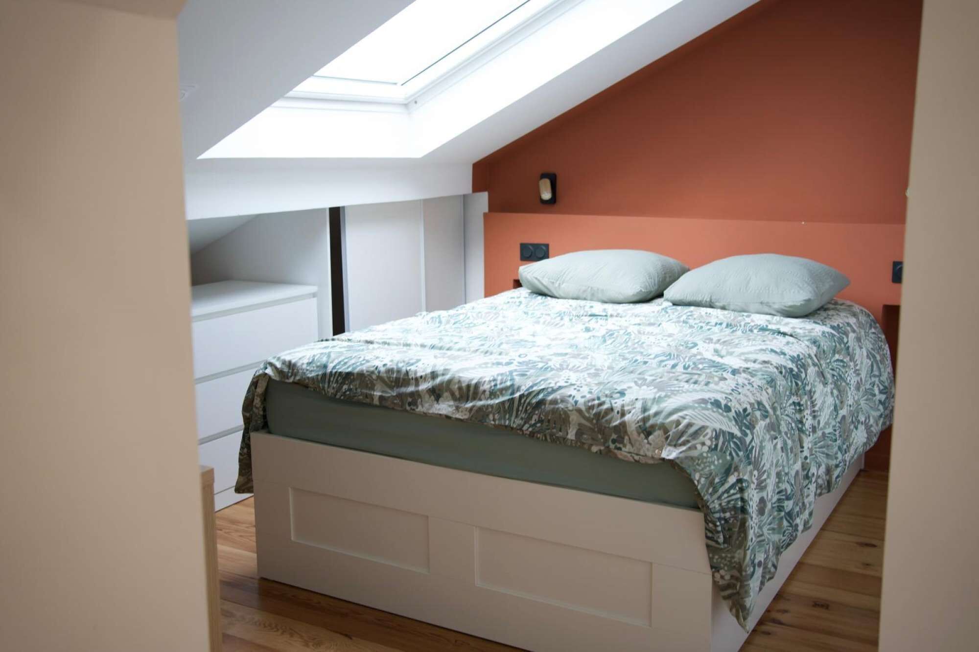 A bedroom with a skylight, a bed with patterned bedding, and a white wardrobe.