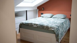 Una camera da letto con un velux, un letto con biancheria a motivi e un armadio bianco.