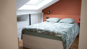 A bedroom with a skylight, a bed with patterned bedding, and a white wardrobe.
