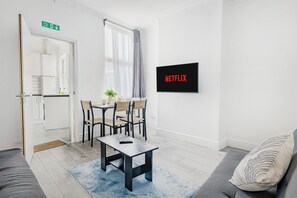 A modern living room with a dining area, a sofa, a coffee table, and a TV mounted on the wall. - NEW! 5BR House, free parking, near City Centre (Nottingham)