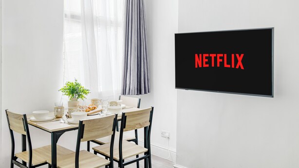 Una zona de menjador amb una taula preparada per a quatre, una planta en test i un televisor fixat a la paret que mostra 'NETFLIX'.