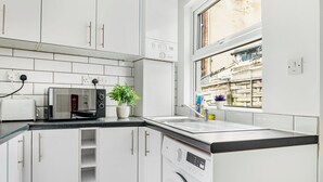 Cuina compacta amb rentadora, microones i finestra amb vista a un edifici.