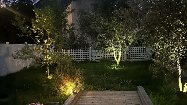 Puinen terassi, jossa on grilli, valkoisen aidan ja puiden ympäröimänä, hämärän taivaan alla.