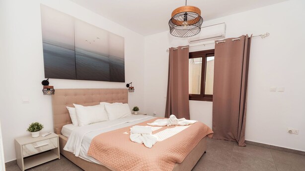 A neatly arranged bedroom with a bed, bedside tables, a wall-mounted artwork, and a window with curtains. - SerenityOne - Centrally located Apt,SO19 (Agia Napa)