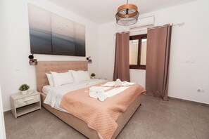 Un dormitorio ordenado con cama, mesitas de noche, un cuadro en la pared y una ventana con cortinas.
