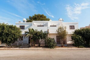 A two-story building with a flat roof, satellite dishes, and a small garden area with trees and shrubs. - SerenityOne - Centrally located Apt,SO19 (Agia Napa)