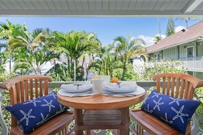 A wooden table with a white plate, a white mug, and a lemon on a wooden chair with a blue starfish pillow. - Kona Islander Inn#336 (Kailua-Kona)
