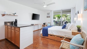 Une chambre compacte comprenant un lit, une petite kitchenette, une télévision et un balcon avec vue sur les palmiers.