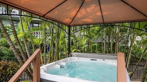 Un bain à remous installé sous une tonnelle, entouré de plantes tropicales.