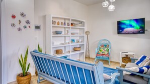 Een woonkamer met een blauwe bank, een witte boekenkast, een televisie en een potplant.