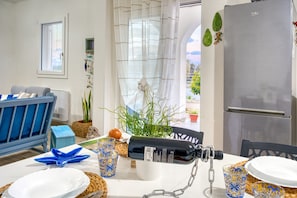 A dining area with a table set for two, a refrigerator, and a view through a window. - Cozy house with little pool and sea view (Leuca)