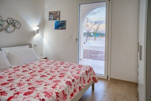 A bedroom with a bed, a door leading to a balcony, and a wall with decorative items. - Cozy house with little pool and sea view (Leuca)