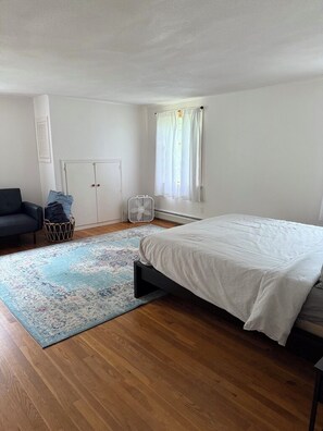 A bedroom with a bed, a chair, a wardrobe, a radiator, and a window with curtains.