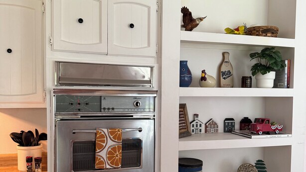 A kitchen with white cabinetry, a stainless steel oven, and a shelf with board games and decorative items. - Spacious Family Getaway Near Sunapee & Dartmouth (Croydon)