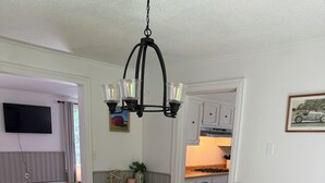 A dining room with a wooden table, black chairs, a chandelier, and a kitchen in the background. - Spacious Family Getaway Near Sunapee & Dartmouth (Croydon)