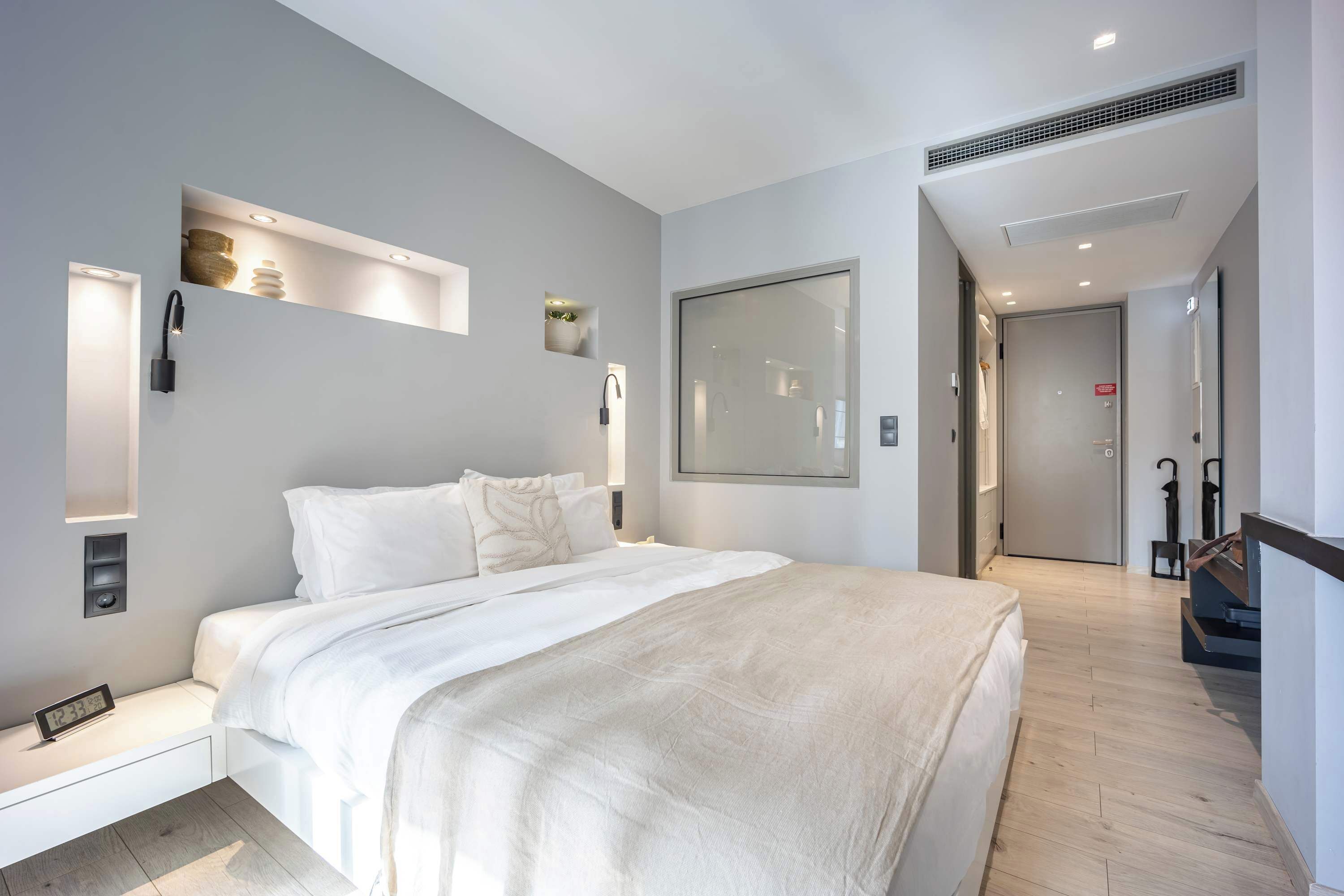 A modern hotel room with a large bed, built-in shelves, a large mirror, and a door leading to another room.