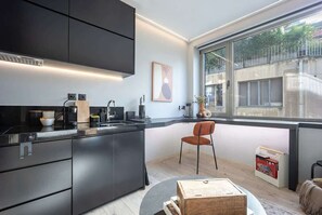 A modern kitchen with dark cabinetry, a built-in oven, and a large window providing a view of the outdoors. - Cozy Spacious Studio Psyri AcropolisView (Athina)