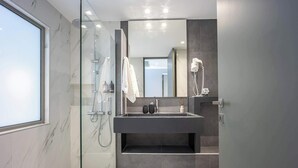 Un baño moderno con ducha envuelta en vidrio, un espejo grande y un lavabo de tonos oscuros.