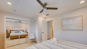Ein Schlafzimmer mit Bett, Deckenventilator, einem Gemälde und Blick durch eine Glastür.