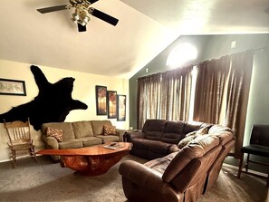 A living room with a sofa, armchair, coffee table, and a mounted animal head.