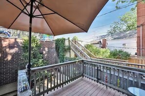 En træterrasse med gelænder i metal, stor parasol og en murstensvæg med grøn bevoksning.
