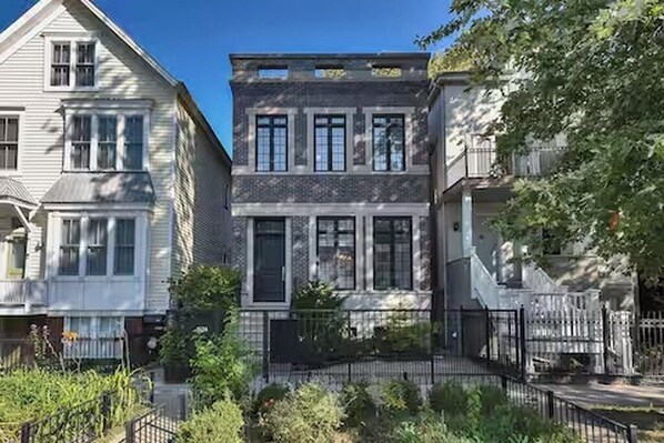 A row of two-story townhouses with a black metal fence in front, a clear sky, and greenery around. - Huge Lakeview Retreat near Wrigley Field with mutliple balconies (Chicago)