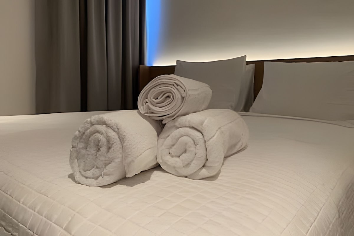 Cama com toalhas brancas dobradas e cabeceira.