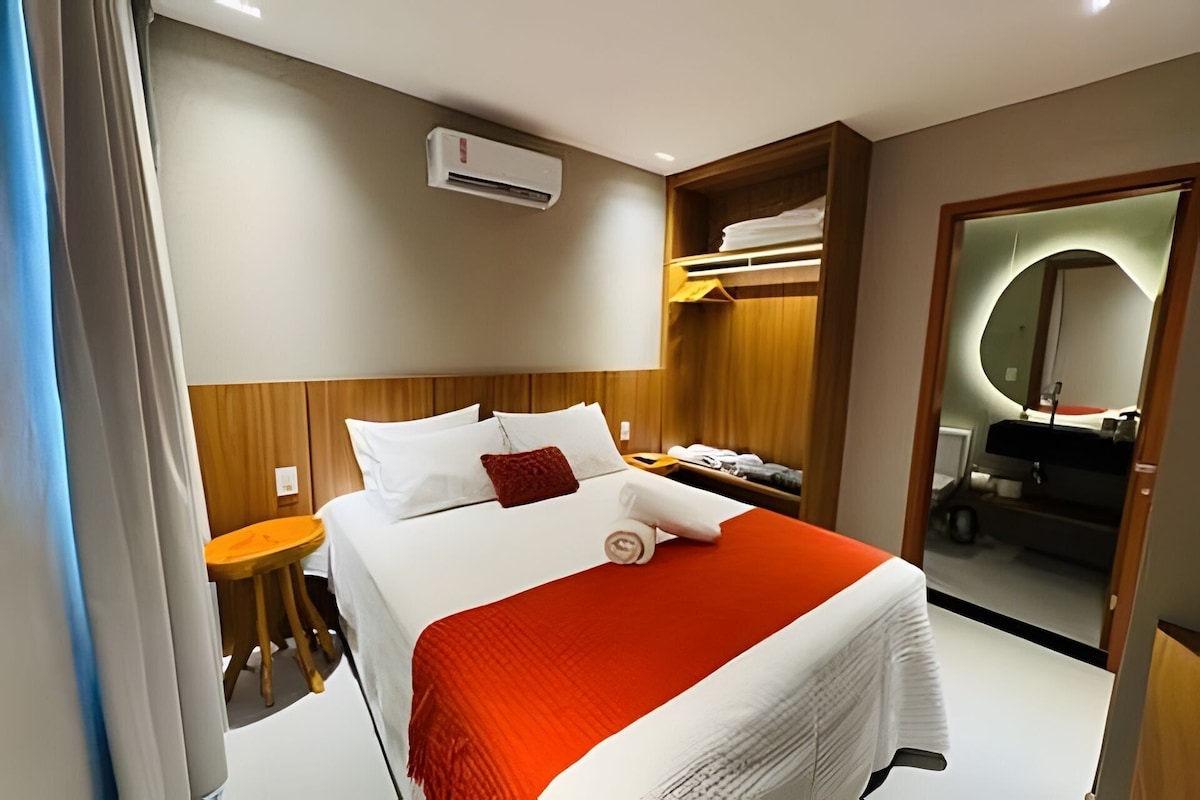 Quarto de hotel com cama, uma pequena mesa, guarda-roupa e espelho.