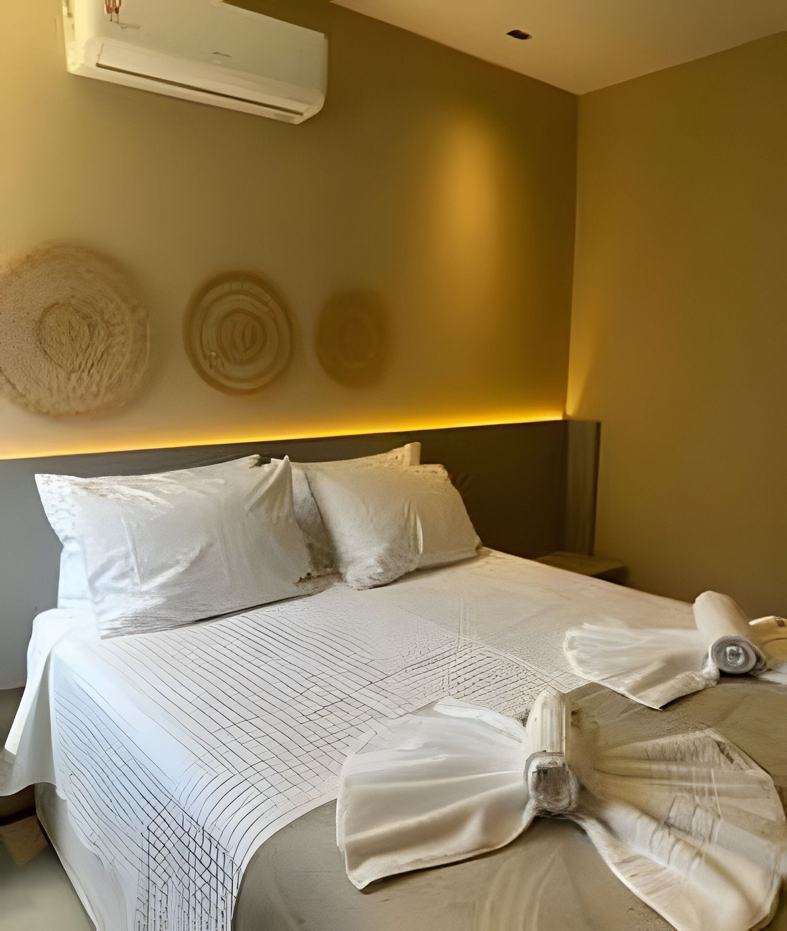 A hotel room with a bed, pillows, a blanket, and a wall-mounted air conditioner.
