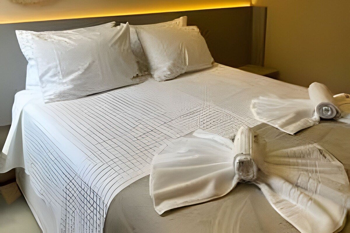 Quarto de hotel com cama, almofadas, manta e ar-condicionado fixado na parede.