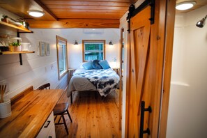 Ein gemütlicher Raum mit Bett, Holzboden, einem Esstisch mit Stühlen, einem Fenster und einer Tür.