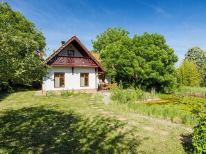 Ein Haus mit Satteldach, einer kleinen Veranda und einem Garten mit Teich.