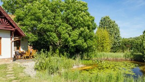 Ein rustikales Haus mit Terrasse, umgeben von üppiger Vegetation und einem Teich.