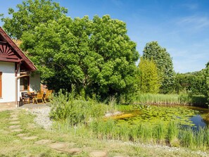 A rustic house with a patio, surrounded by lush greenery and a pond. - Villa Canela by Interhome (Pécsely)