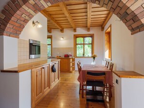 A kitchen with wooden cabinets, a built-in oven, and a dining area with a checkered tablecloth. - Villa Canela by Interhome (Pécsely)