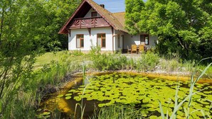 Ein Haus mit einem Ziegeldach, einer Veranda mit Stühlen und einem Teich mit Seerosen.