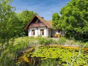 A house with a tiled roof, a porch with chairs, and a pond with lily pads. - Villa Canela by Interhome (Pécsely)