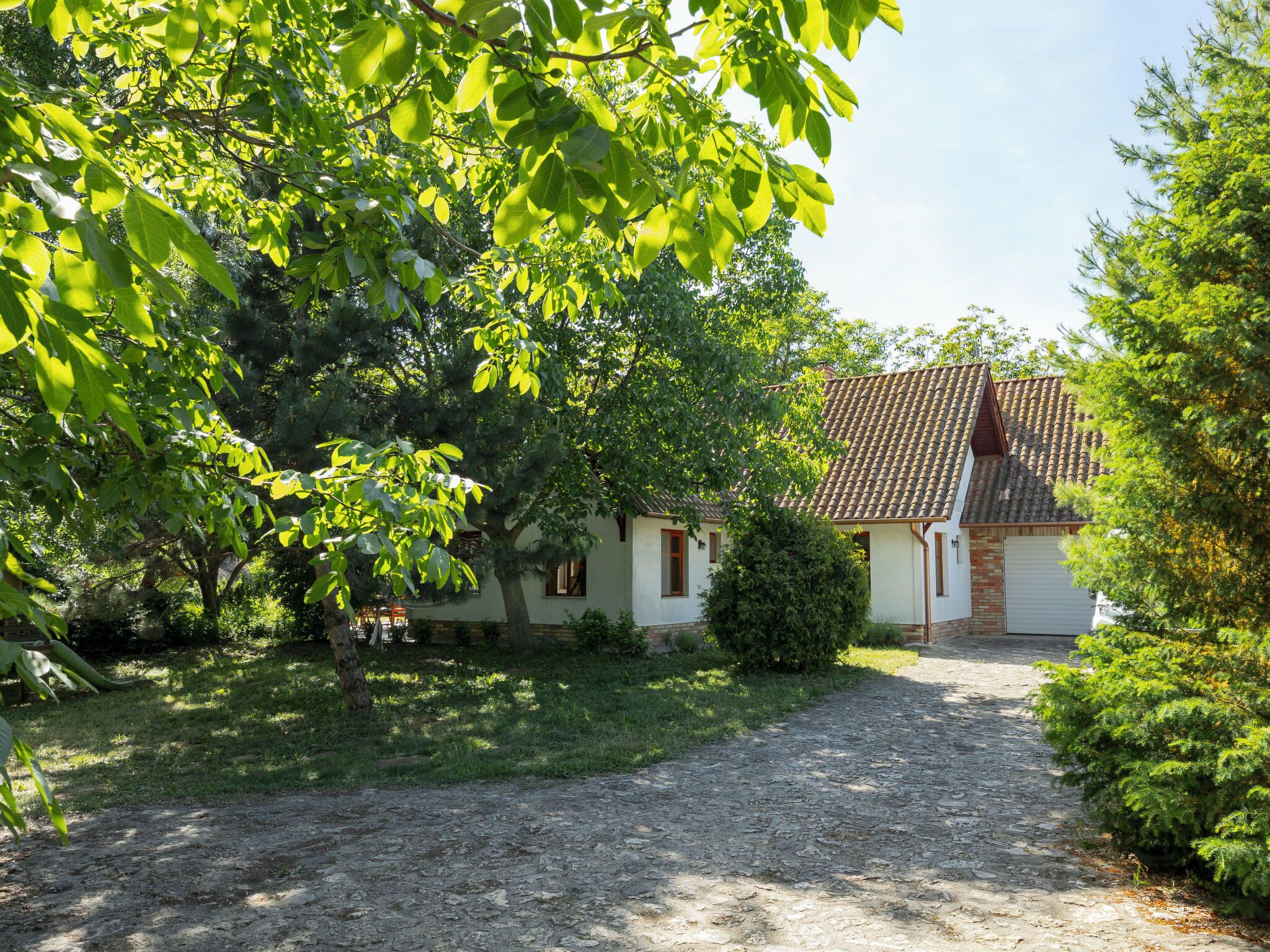 A house with a tiled roof, a gravel driveway, and surrounding greenery.