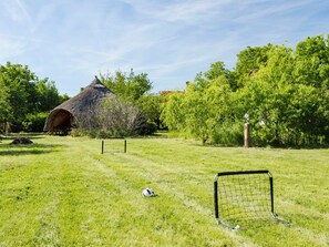 Eine Wiese mit einem Fußballtor, einem Gebäude mit einem Strohdach und Bäumen.