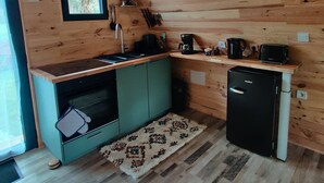 A compact kitchen with wooden walls, a window, a sink, a stove, a refrigerator, and a coffee maker.