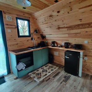 Une cuisine de taille réduite avec des murs en bois, une fenêtre, un évier, une cuisinière, un réfrigérateur et une machine à café.