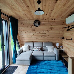 L’intérieur d’un chalet confortable, avec un canapé, une horloge et une fenêtre avec des rideaux.