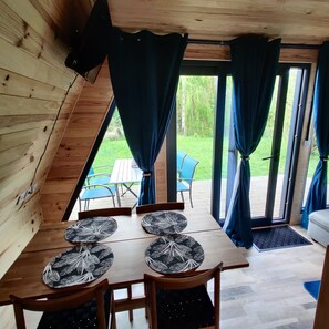 A wooden interior with a dining table, chairs, and curtains. - Enjoy the sounds of nature when you stay in this unique wooden Tipi. (Vivy)
